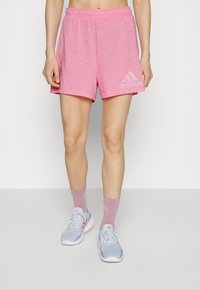 Shorts de sport roses avec un motif moucheté, taille élastique et logo Adidas sur le côté. Assortis avec des baskets bleu clair et des chaussettes roses.