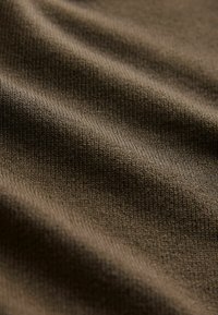 Braunes Textilgewebe mit geripptem Strickmuster, das weiche Wellen und Tiefe zeigt und sich für Bekleidungs- oder Polsteranwendungen eignet.