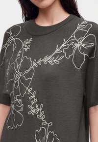 Haut en maille gris foncé à manches courtes avec de grands motifs floraux et de vignes blancs brodés sur la poitrine et les épaules.