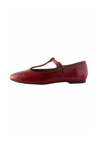 Zapato plano rojo estilo Mary Jane con puntera redondeada y una correa en la parte superior. El zapato tiene un tacón bajo y un acabado suave.