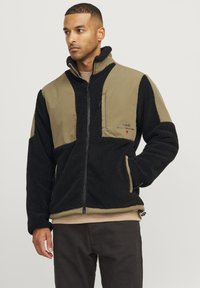 Giacca in pile nera e verde oliva, con zip frontale, colletto alto, due tasche frontali e texture a coste sulle maniche.