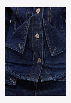 Veste en denim bleu foncé avec boutons-pression argentés et coutures contrastantes jaunes sur les rabats pliés et les coutures.