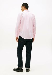 Lichtroze button-up shirt met lange mouwen, rugplooidetail, gedragen met donkerblauwe jeans en zwarte schoenen. Eenvoudig, strak ontwerp.