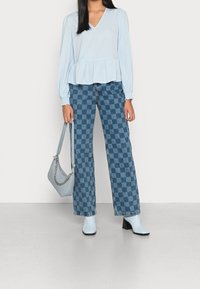 Light blue peplum blouse with long sleeves, paired with patterned wide-leg jeans featuring a checkered blue design and blue ankle boots.