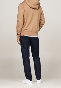 Beige huvtröja, mörkblå jeans, vita sneakers. Slät tyg, figurnära passform, minimalistisk design, synlig sömnad på jeansen.