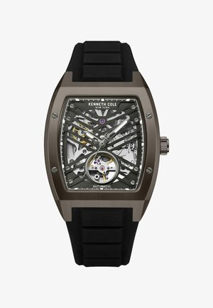 Automatische Armbanduhr mit einem schwarzen Gummiarmband, dunkelmetallischem Gehäuse, Skelettzifferblatt, das Zahnräder zeigt, silbernen Akzenten und lila Details.