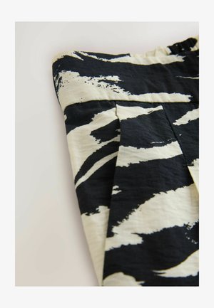 Sort-hvid zebra-stribet stof med en tekstureret finish. Har plisseringer og en elastik i taljen for justerbar pasform.