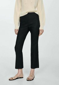 Zwarte op maat gemaakte broeken met een rechte snit, voorzien van een gladde textuur en een hoge taille, gecombineerd met een crèmekleurige gebreide trui en sandalen.