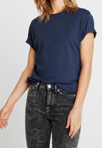 Mörkblå bomulls t-shirt med uppvikta korta ärmar, i kombination med urblekta svarta denimjeans med hög midja och knappstängning fram.