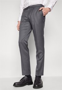 Gray tailored trousers in a smooth fabric with a slim fit, featuring side pockets and a flat front. Paired with black dress shoes.