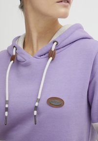Felpa viola con cappuccio e cordoncino, caratterizzata da dettagli in corda naturale e un'etichetta del logo marrone. Tessuto morbido e liscio con un interno chiaro a contrasto.