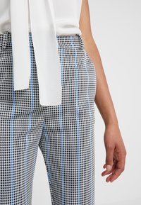 Pantaloni in tessuto houndstooth bianco e nero con strisce blu; con vita alta e tasche laterali. Tessuto di consistenza liscia.