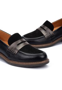 Mocasines de cuero negro con acentos de ante, que cuentan con un acabado texturizado, costuras en marrón contrastante y un diseño de punta suave y redondeada.