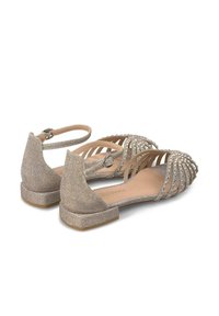Sandales dorées scintillantes au design ouvert, ornées de strass, avec un talon fermé et une sangle ajustable à la cheville. Semelle plate.