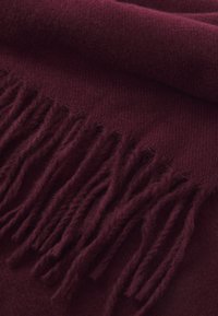 Écharpe bordeaux en tissu doux, présentant une texture lisse et des bords frangés, mettant en valeur une couleur riche et profonde.