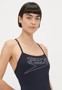 Μαύρο μαγιό με λεπτές τιράντες στους ώμους. Διαθέτει λευκό λογότυπο "SPEEDO" και καμπυλωτό σχέδιο στο μπροστινό μέρος. Λείο ύφασμα.