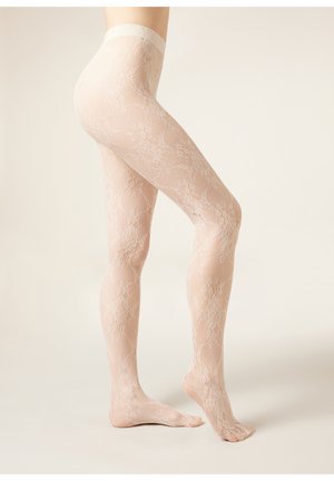 Benen met doorschijnende huidkleurige kousen van kant met een bloemenpatroon, staand met één voet plat op de grond en de andere licht op de tenen.