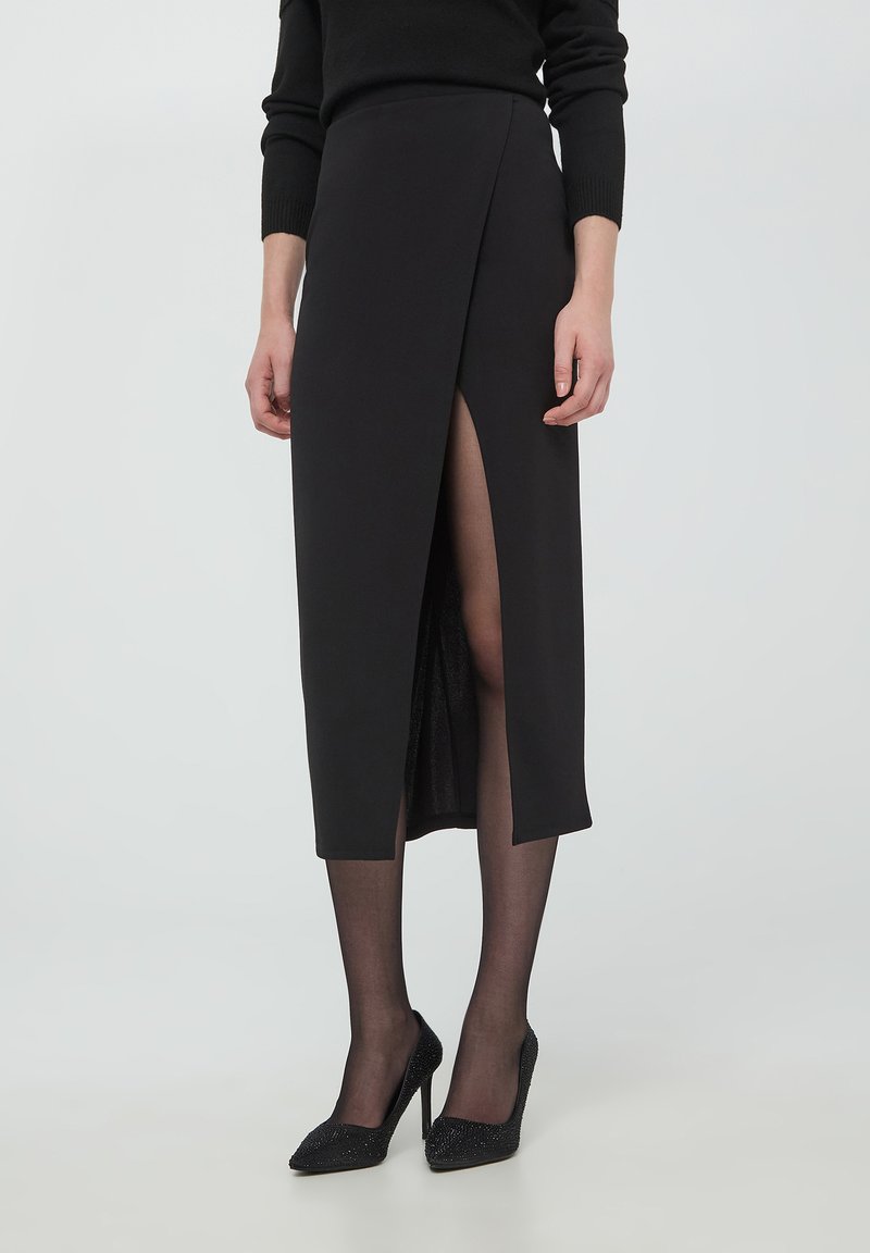 Gonna nera a matita con un'alta scollatura, texture liscia, lunghezza a metà polpaccio, abbinata a tacchi alti neri e lucidi.