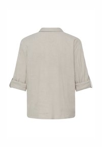 Camisa beige de manga larga con las mangas remangadas, cuello sencillo y un corte suelto y recto mostrada desde atrás.