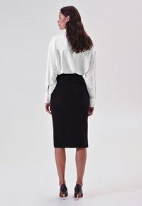 Blusa bianca con maniche lunghe, gonna a tubino nera e tacchi neri con un accento dorato. Tessuto liscio, silhouette aderente.