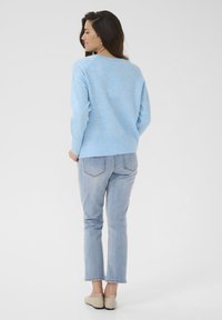 Pull en tricot bleu clair à coupe décontractée, avec des manches raglan et un ourlet côtelé, associé à un jean bleu clair et des chaussures slip-on beiges.