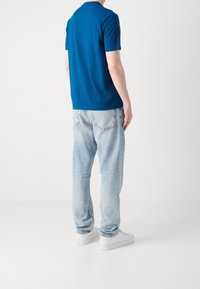 Modrá bavlněná tričko s krátkým rukávem, spárované s lehkými džíny, s klasickým střihem a jemným vyblednutím. Bílí tenisky dotvářejí celkový vzhled.