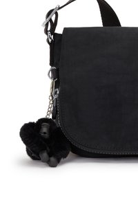 Borsa a tracolla nera in tessuto con pattina e un piccolo portachiavi gorilla peluche nero attaccato al cursore della cerniera.