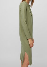Robe olive verte à manches longues avec un col, des boutons, des fentes sur les côtés et une silhouette droite en tissu doux.
