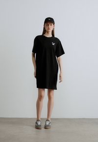 Čierne oversize tričko-šaty vyrobené z bavlny, s malým logom na hrudi. Dopĺňa ich čierna čiapka a sivé tenisky.