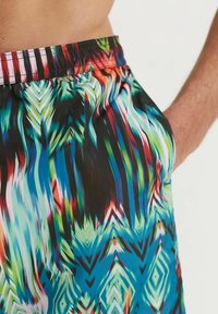 Costumi da bagno multicolori presentano un motivo astratto dinamico in blu, verde, rosso e nero, con vita elastica e tasca laterale.