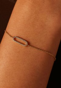 Gouden schakelsieraad met een langwerpige ovale schakel en heldere accenten. De ketting is delicaat, met een zachte textuur tegen de huid.