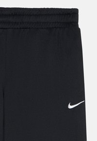 Juodos sportinės kelnės su elastingu juosmeniu ir baltu Nike swoosh logotipu ant šlaunies.
