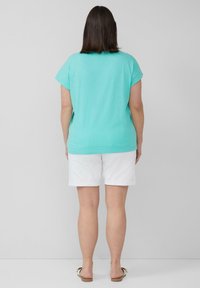 Een turquoise shirt met korte mouwen, gecombineerd met een witte short. Het shirt heeft een relaxte pasvorm en de shorts zijn knie-length met een opgerolde zoom.