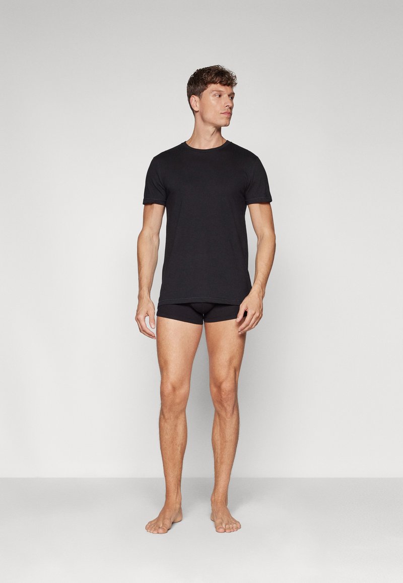 Svart bomull t-skjorte med korte ermer, rund hals og en noe figursydd design, sammen med svarte boxershorts. Barfot i stående posisjon.