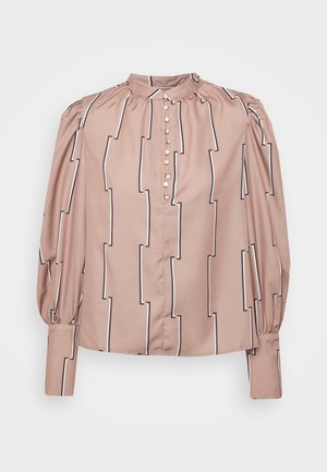 Blouse beige à manches longues avec des rayures géométriques verticales noires et blanches, patte de boutonnage à l'avant, épaules froncées et larges poignets.