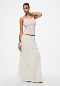 Světle růžový žebrovaný top na ramínka s mašlí, doplněný volnou, vrstvenou maxi sukní v přírodní barvě s elastickým pasem.
