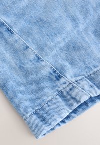 Tissu en denim bleu clair avec des coutures visibles et un ourlet plié.