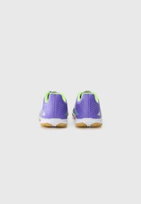 Zapatillas deportivas moradas con acentos verdes, parte superior texturizada y suela blanca flexible. Incluyen orificios de ventilación y un diseño de talón curvado.