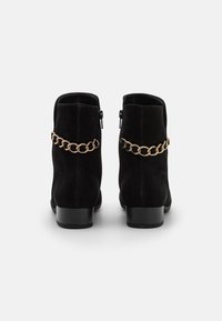 Svarta mocka anklarstövlar med ett guld kedjeaccent, fyrkantig klack, sidodragkedjor och en jämn, strukturerad yta.