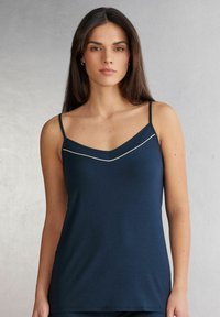 Marinblå ärmlös topp med v-ringad design och kontrasterande vit kant längs halsringningen, tillverkad av mjukt jersey-tyg.