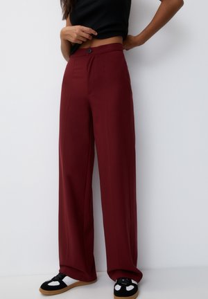 Personne portant un pantalon bordeaux taille haute à jambes larges, un top court noir et des baskets noires et blanches avec semelles en gomme.