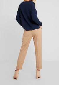 Granatowy sweter o fakturze z luźnym krojem, w połączeniu z beżowymi, dopasowanymi spodniami z podwiniętymi nogawkami oraz jasnobeżowymi wysokimi botkami na obcasie.