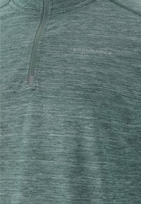 Groene textuur pullover top met een ritsluiting, gemaakt van een lichtgewicht stof met subtiele gemêleerde patronen, met het merk "ENDURANCE."