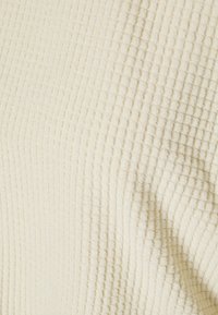Tela de color crema texturizada con un patrón de cuadrícula. El material parece suave y ligeramente aterciopelado, reflejando un sutil brillo.