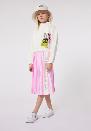 Witte sweatshirt met grafische details, roze geplooide rok met strepen en witte sneakers met een logo. Het model draagt ook een witte bucket hat.