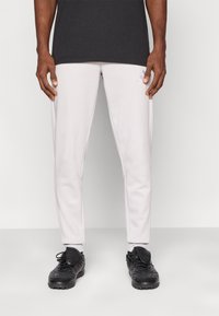 Pantalones deportivos gris claro con un corte estrecho, hechos de tela suave, con bolsillos laterales y un pequeño logo en la cadera izquierda.