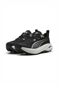 Zapatillas deportivas negras con parte superior de malla texturizada, acentos reflectantes y una suela blanca gruesa. Presentan cordones con un patrón y una lengüeta.