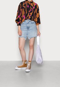 Mønstret langærmet bluse i flere farver med abstrakt mønster, denimnederdel med frynset kant, brune høj-top sneakers og en lys lilla skuldertaske.