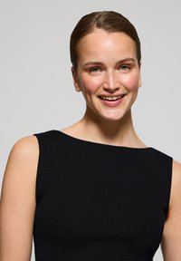 Svart ribbad klänning med båt-urringning och ärmlöst design. Slät textur, figurnära passform och minimalistisk stil framhäver plagget.