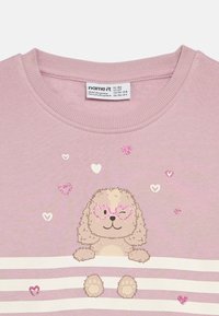 Vaaleanpunainen collegepaita, jossa on sarjakuvamainen pentukoira, jolla on vaaleanpunaiset sydämenmuotoiset aurinkolasit, ympärillään pieniä sydämiä ja vaakasuoria valkoisia raitoja.